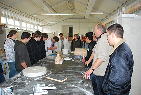 Das Bild zeigt eine Schulklasse beim Rundgang. Eine Stuckateurarbeit wird begutachtet.